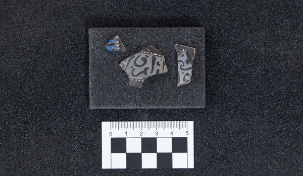 A tiny fragment of historic Islamic glass on a table with a ruler beside it